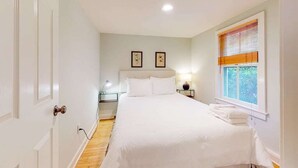 Ein Schlafzimmer mit Bett, Nachttischen, Fenster mit Jalousien und einer Tür.