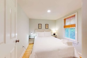 A bedroom with a bed, bedside tables, a nightstand, a window with blinds, and a door. - Town of Rehoboth Beach home near beach, tennis courts, grill, patio, W/D, WiFi (Rehoboth Beach)