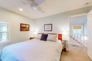 A bedroom with a bed, a ceiling fan, two bedside tables with lamps, a framed picture on the wall, and a staircase leading to an upper floor. - Town of Rehoboth Beach home near beach, tennis courts, grill, patio, W/D, WiFi (Rehoboth Beach)