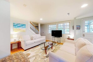 A living room with a white sofa, a glass coffee table, a TV, and a staircase. - Town of Rehoboth Beach home near beach, tennis courts, grill, patio, W/D, WiFi (Rehoboth Beach)