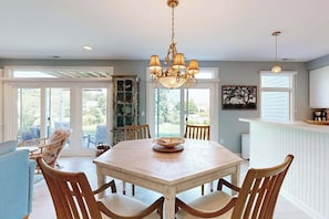 A dining area with a wooden table, chairs, a chandelier, and a view through large windows. - Spring Lake Condo with patio, free WIFI, W/D, shared pool (Rehoboth Beach)