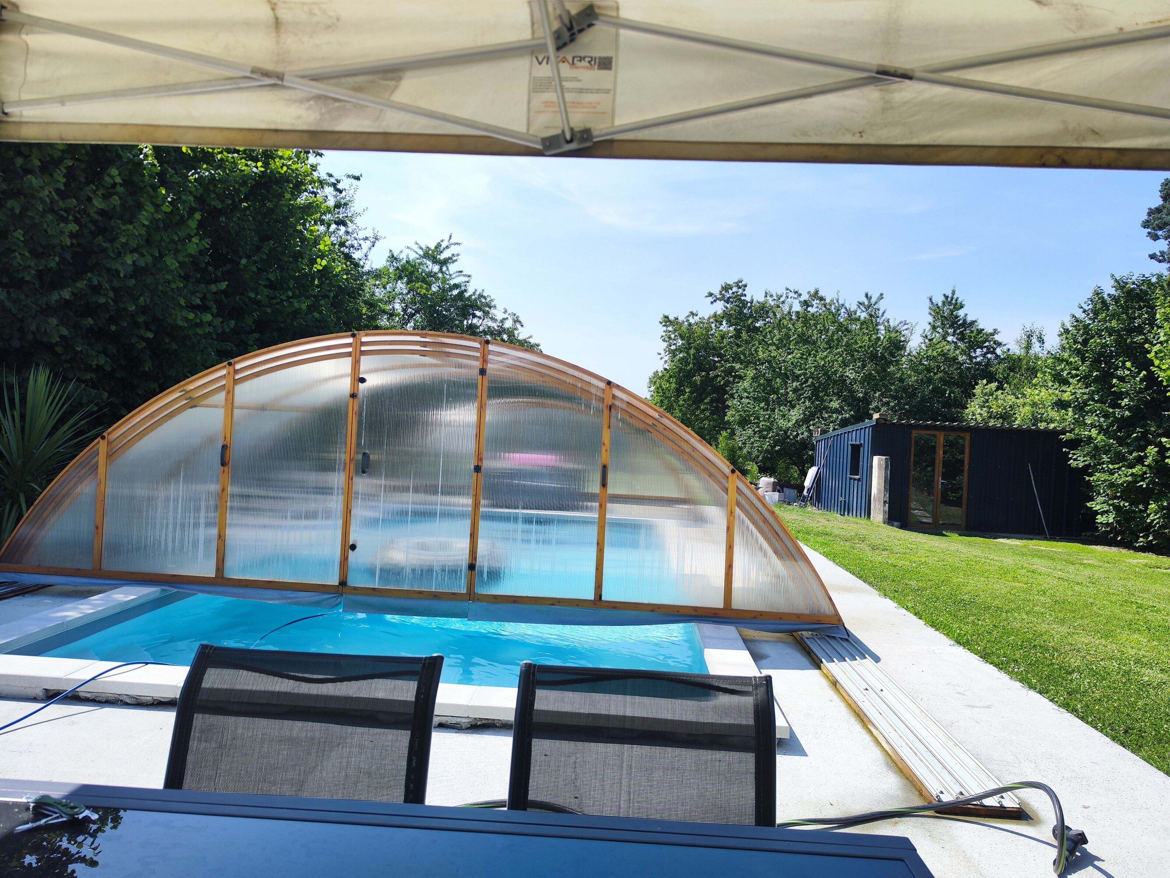 Une piscine entourée d’une structure en verre et bordée d’une terrasse couverte.