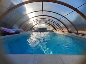 An indoor swimming pool with clear water, a pink float, and a bench. - Chez Sandrine Guest Rooms and Table d'Hôtes with Pool (Gray-la-Ville)