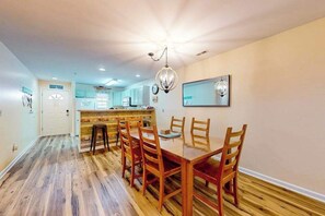 Un coin repas avec une table et des chaises en bois, une cuisine en arrière-plan et un lustre.