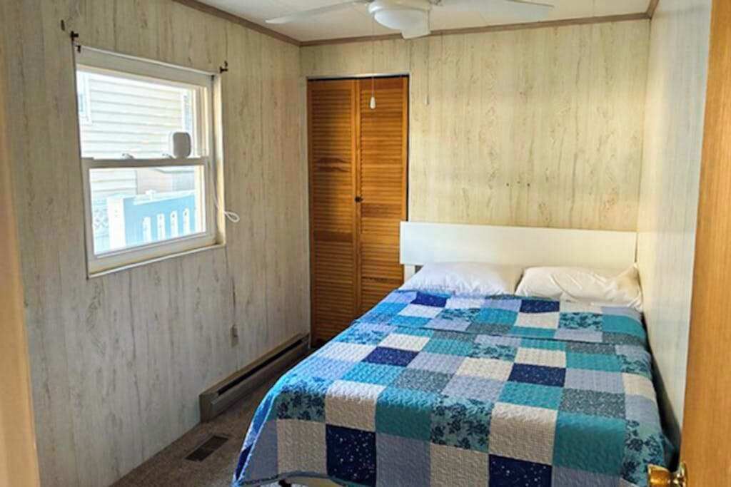 A bedroom with a wooden wardrobe, a quilted bedspread, and a window with blinds.