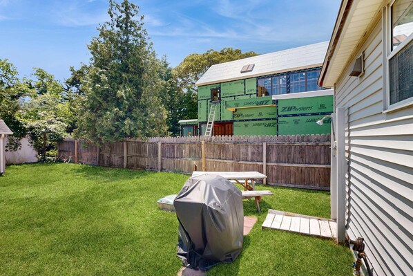 A backyard with a covered grill, a wooden deck, and a house under construction with insulation visible. - Dog-friendly Rehoboth Beach gem steps from beach & boardwalk with fast WiFi (Rehoboth Beach)