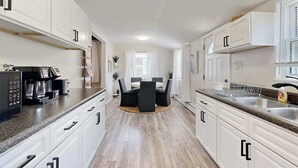 A modern kitchen with white cabinets, a dining area with a table and chairs, and a coffee machine. - Dog-friendly Rehoboth Beach gem steps from beach & boardwalk with fast WiFi (Rehoboth Beach)