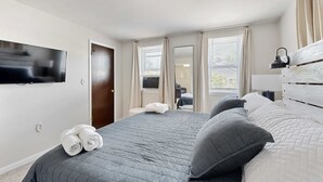 A bedroom with a bed, a TV mounted on the wall, and a window with curtains. - Dog-friendly Rehoboth Beach gem steps from beach & boardwalk with fast WiFi (Rehoboth Beach)