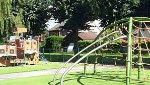 A playground with a climbing structure, slides, and a fenced area. - L'écrin de l'abreuvoir – Cozy Ground-Floor Retreat in Marnay Near Besançon (Marnay)