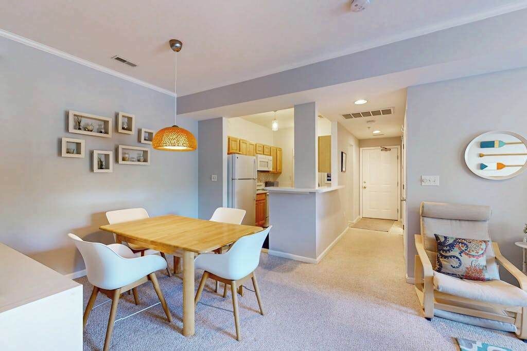 Une cuisine moderne avec des meubles en bois et un four à micro-ondes, un coin repas avec une table en bois et des chaises blanches, et un couloir menant à une porte.