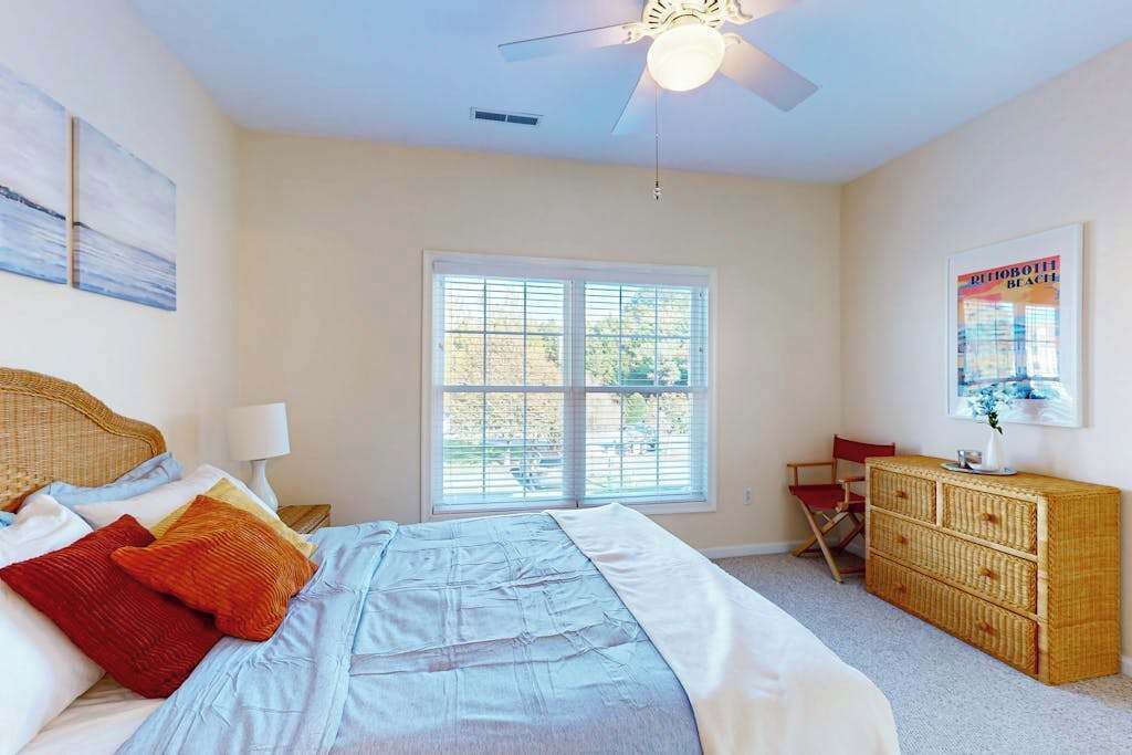 Ein Schlafzimmer mit Bett, Kommode, Stuhl, Fenster und Deckenventilator.