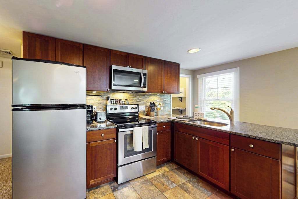 A kitchen with wooden cabinets, stainless steel appliances, a microwave, oven, and a sink.