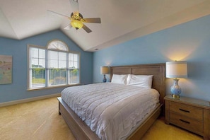 Un dormitorio con cama, mesita de noche, lámpara, ventilador de techo y ventana con persianas.