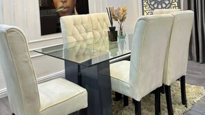 A dining area with a glass table, four upholstered chairs, a decorative vase, and a patterned wall. - Two Bedroom Luxury Apartment in Wuse 2 (Abuja)