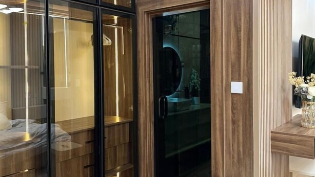 A modern room with a built-in wardrobe, a glass door leading to a bathroom, and a small trash bin. - Two Bedroom Luxury Apartment in Wuse 2 (Abuja)