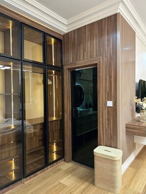 A modern room with a built-in wardrobe, a glass door leading to a bathroom, and a small trash bin. - Two Bedroom Luxury Apartment in Wuse 2 (Abuja)