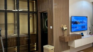 A modern hotel room with a glass partition, a wooden panel wall, a mounted TV, and a small trash bin. - Two Bedroom Luxury Apartment in Wuse 2 (Abuja)