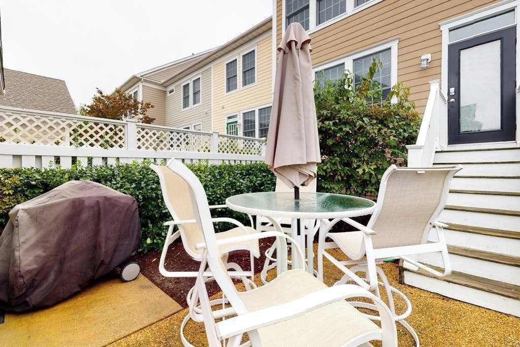 Une terrasse avec une table et des chaises, un barbecue abrité et une clôture blanche.