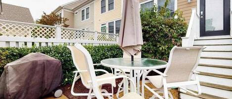 Une terrasse avec une table et des chaises, un barbecue abrité et une clôture blanche.