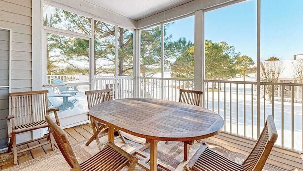 Un espacio al aire libre cubierto con mesa y sillas de madera, ventanas amplias y vistas al exterior.
