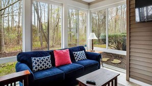 A sunroom with a blue sofa, a lamp, and a TV on the wall. - Sea Colony Tennis townhouse with board games, & tennis court (Bethany Beach)