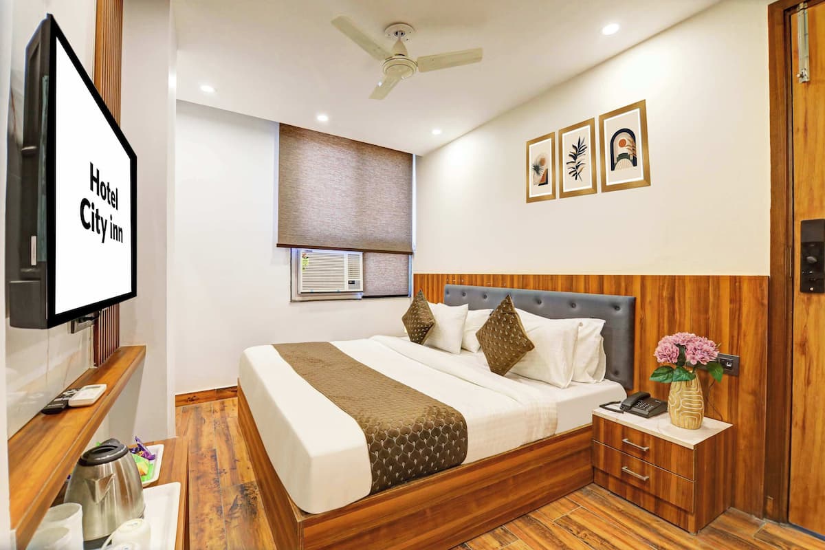 A hotel room with a bed, bedside table, TV, and a wooden floor.