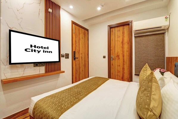 A hotel room with a bed, wooden doors, an air conditioning unit, and a television displaying 'Hotel City Inn'.