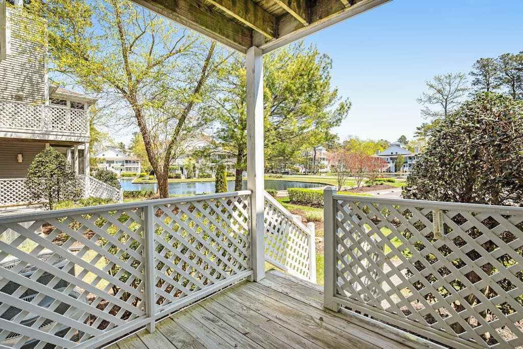 Une terrasse en bois avec une balustrade blanche à claire-voie, un espace abrité et une vue sur un quartier résidentiel avec des maisons et des arbres.