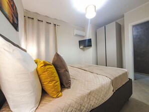 A bedroom with a bed, a flat-screen TV, an air conditioning unit, and a door. - Siciliandò by Interhome (Terrasini)
