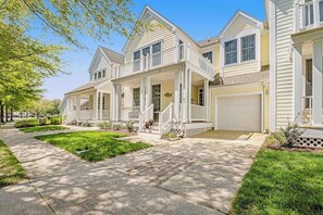Ein zweistöckiges Wohnhaus mit überdachter Veranda, Garage und gepflegtem Rasen.