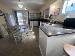 A kitchen with a granite countertop, white cabinets, and a dining area with a wooden table and chairs. - NEW - Surf Manor | 4BR Beach House • 4 Homes to Beach Access • Deck, BBQ & Games (Seaside)