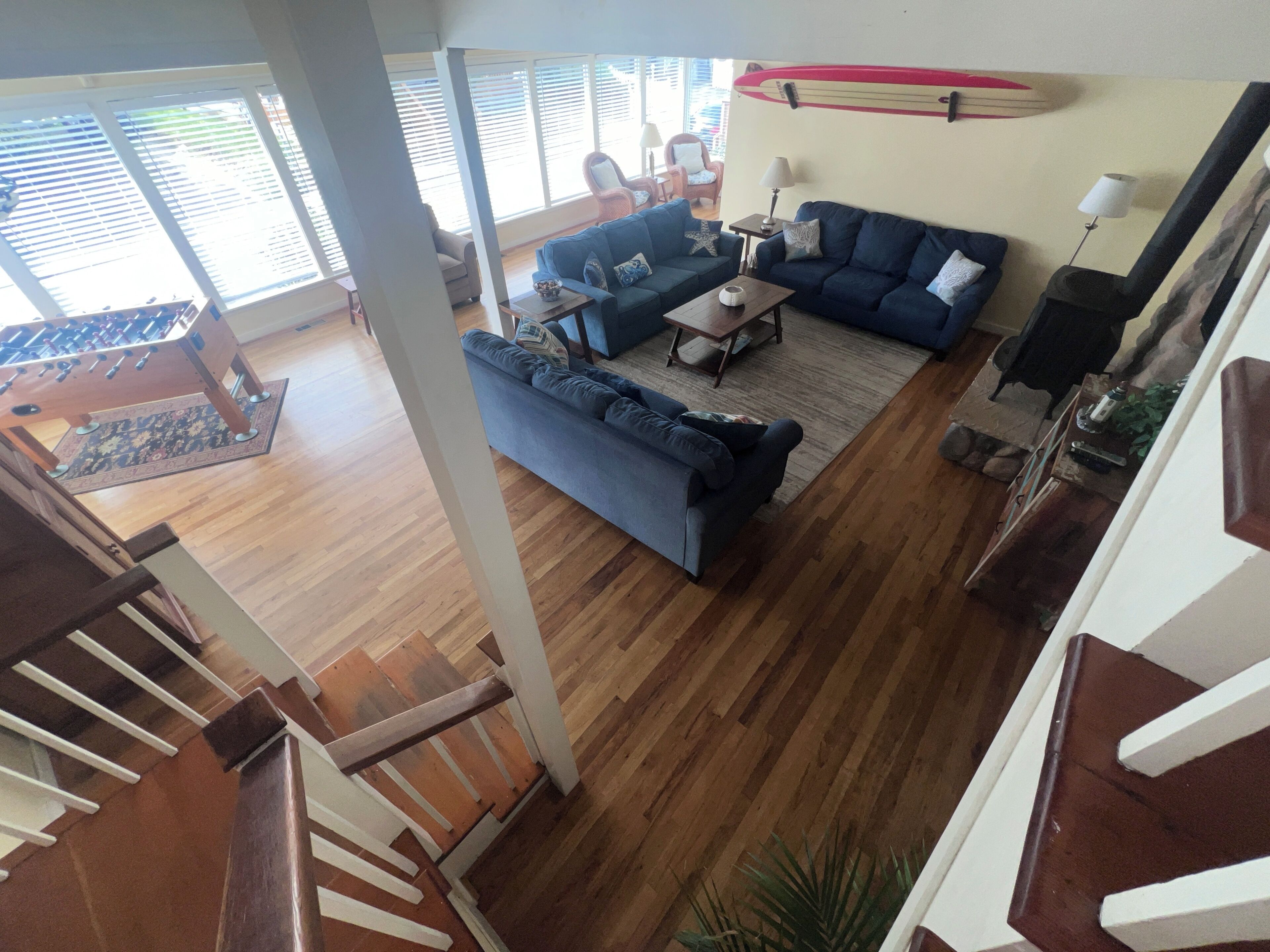 Un vaste espace de vie doté d’un plancher en bois, d’un canapé bleu, d  ’une table basse et d’une planche de surf accrochée au mur.