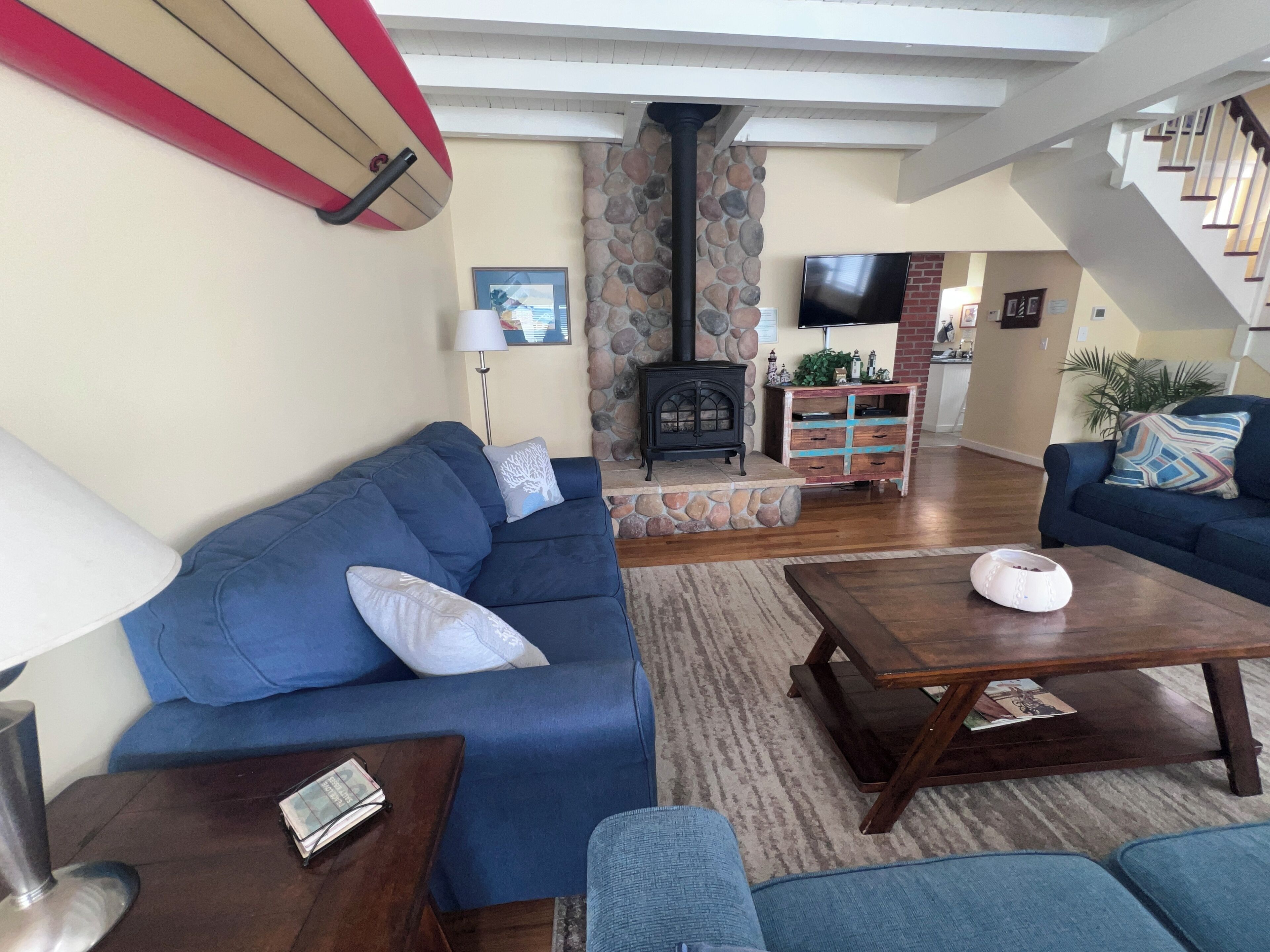 A living room with a blue sofa, a wooden coffee table, a stone fireplace, and a staircase leading to another level.