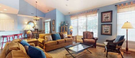 A spacious living room with a high ceiling, a ceiling fan, and a large window with curtains.