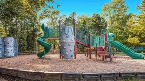 A playground with climbing structures, slides, and a wooden fence. - Sea Colony Tennis second-floor condo with fireplace, gym, & tennis court (Bethany Beach)