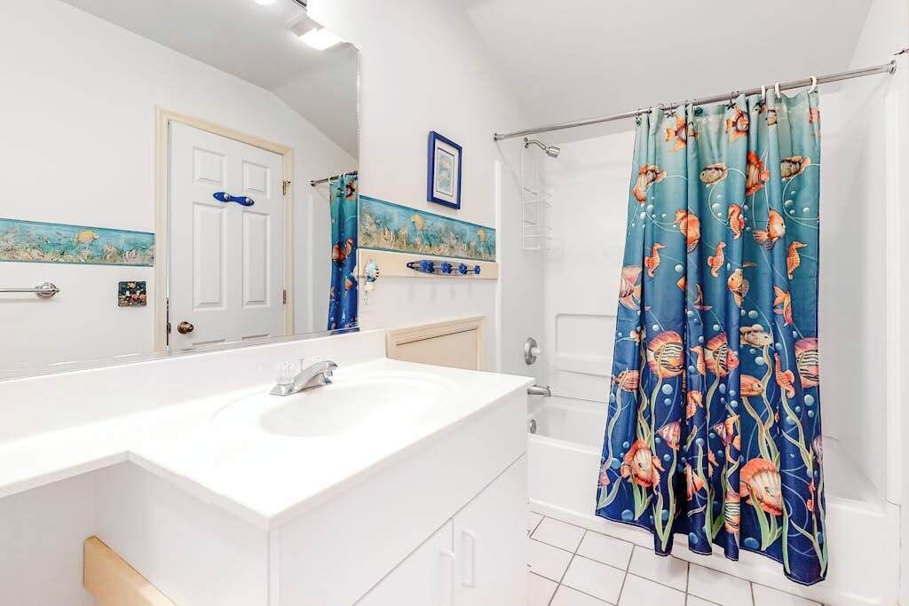Ein Badezimmer mit einem weißen Waschbecken, einer Badewanne und einem Duschvorhang mit Fischmuster.