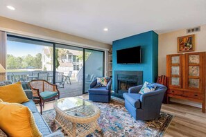 Una sala de estar con sofá, sillones, una mesa de centro de vidrio, chimenea y televisor montado en la pared.