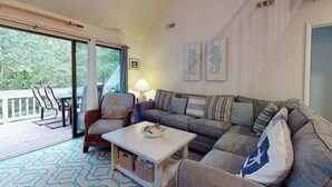 Ein Wohnzimmer mit einer Couch, Sesseln, einem Couchtisch und einem Balkon mit Gartenmöbeln.