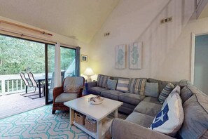 A living room with a sofa, armchairs, a coffee table, and a balcony with outdoor furniture. - 2nd-floor Sea Colony Tennis condo with pool & gym access (Bethany Beach)