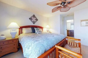 Une chambre à coucher comprenant un lit, des tables de chevet, un ventilateur de plafond, une œuvre d’art accrochée au mur et un miroir.