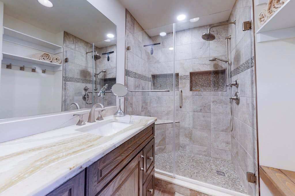 A modern bathroom with a large mirror, a shower with a glass door, and a vanity with a sink.