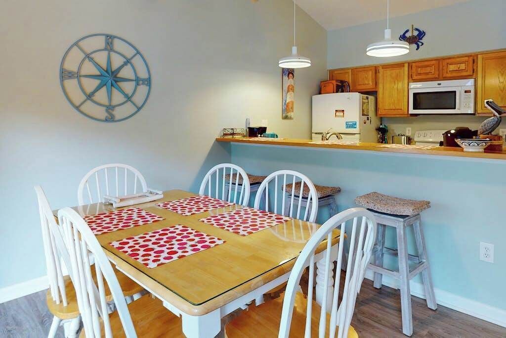 A dining area with a wooden table and white chairs, a kitchen with wooden cabinets and appliances, and a wall-mounted compass decoration.