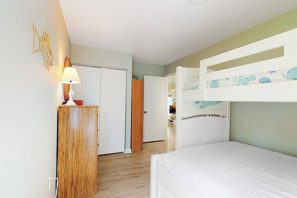 A room with bunk beds, a wooden cabinet, a lamp, and a door leading to another room.