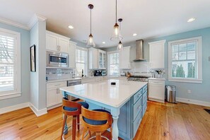 A modern kitchen with white cabinets, a large island, and pendant lighting. - Coastal Elegance: Retreat Two Blocks from the Sand (Rehoboth Beach)