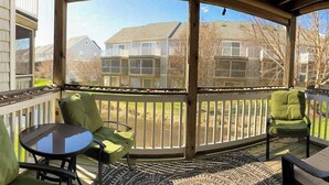 A covered outdoor area with a table and chairs, a patterned rug, and a view of residential buildings. - Canal Landing townhouse w/community pool, patio, close to restaurants (Rehoboth Beach)