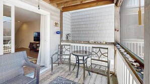 A covered outdoor area with a table and chairs, a view of the interior, and a window with a railing. - Canal Landing townhouse w/community pool, patio, close to restaurants (Rehoboth Beach)