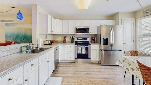 A modern kitchen with white cabinets, stainless steel appliances, and a dining area with a table and chairs. - Canal Landing townhouse w/community pool, patio, close to restaurants (Rehoboth Beach)