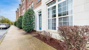Een rij herenhuizen met een trottoir, geparkeerde auto's en een verzorgde haag.