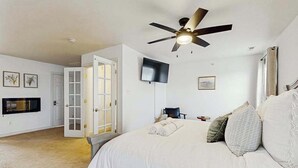 Een slaapkamer met een bed, een plafondventilator, een televisie en een deur naar een andere kamer.