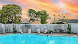 Uma piscina com espreguiçadeiras e guarda-sóis, cercada por uma vedação de madeira.
